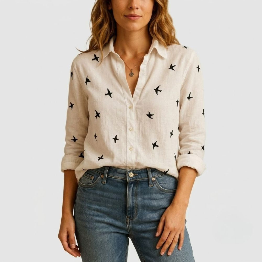 Blusa de linho bege com estampa de pássaros pretos, gola clássica, botões frontais e corte solto.