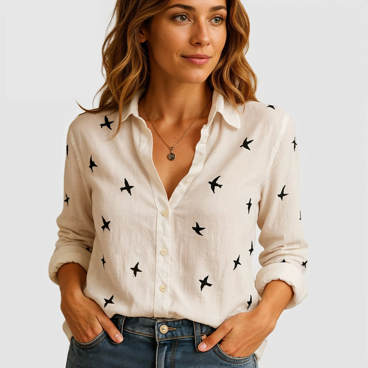 Blusa feminina de linho bege com estampa de pássaros pretos, gola clássica e botões frontais em corte solto.