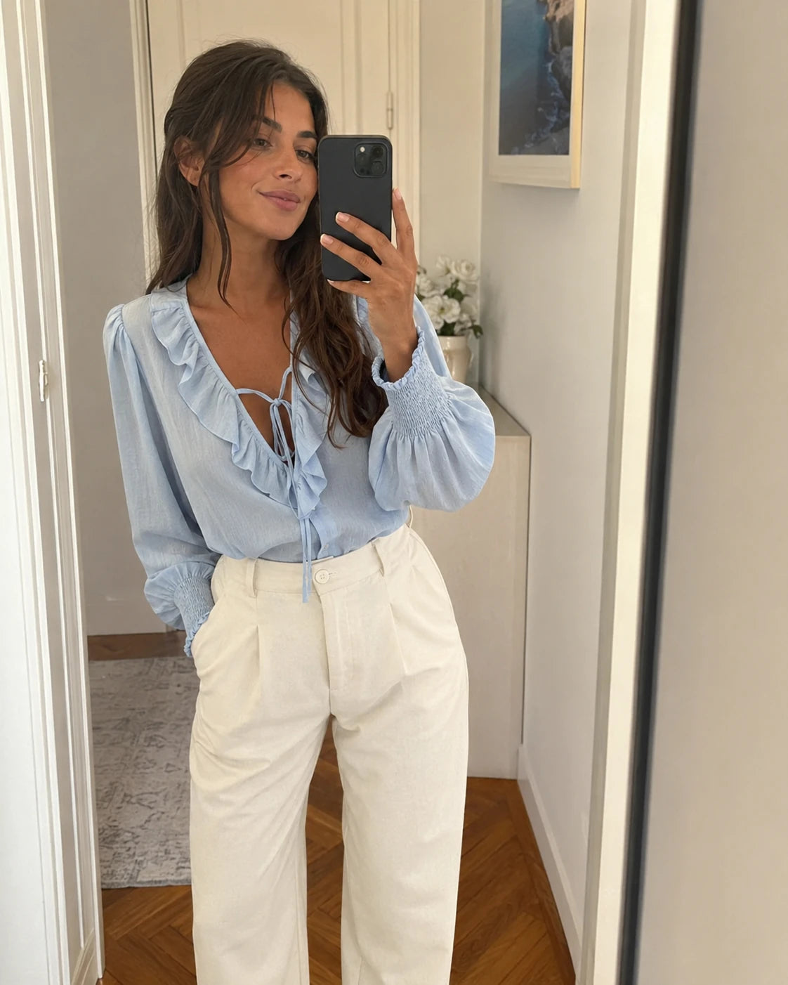 Mulher com blusa azul-clara e calças brancas num autorretrato ao espelho